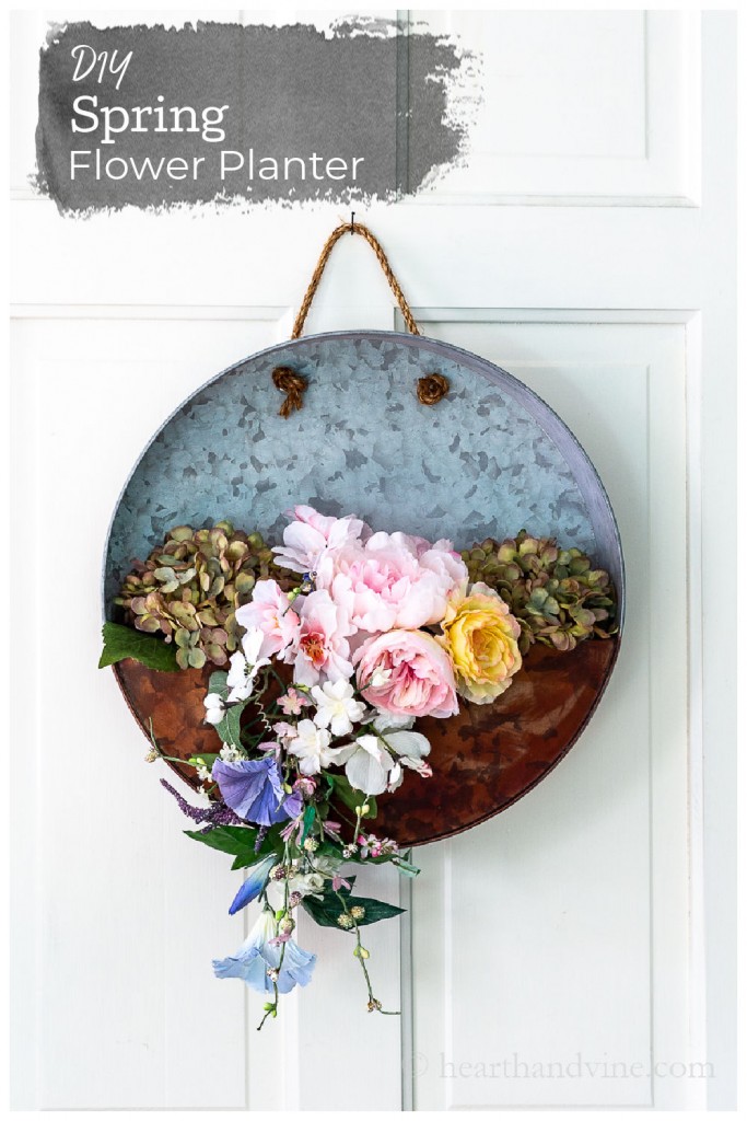 Galvanized hanging planter with faux spring flowers on a white door.