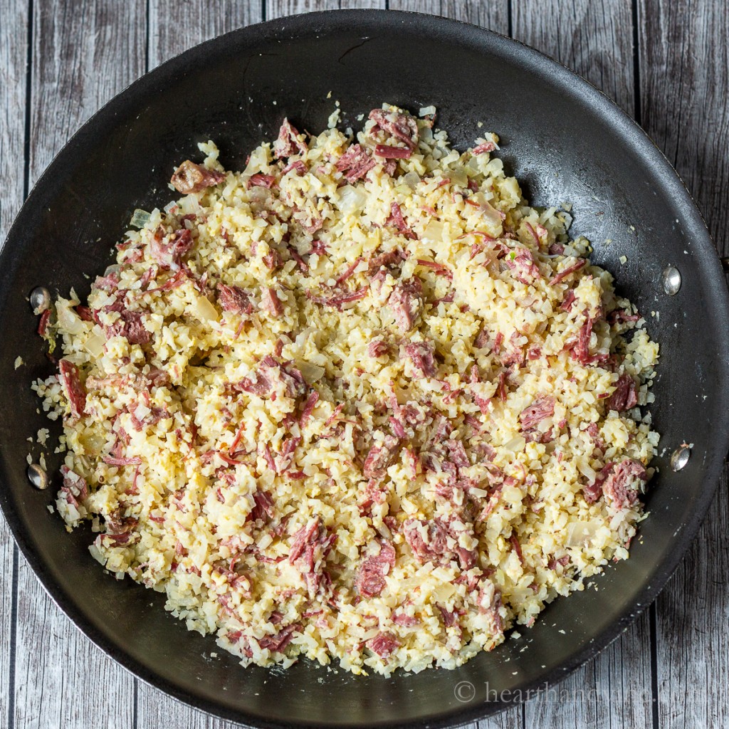 Large black skillet with cauliflower rice, corned beef and eggs.