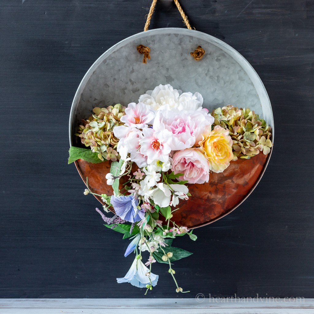 Hanging galvanized metal planter with spring flowers on a black background.