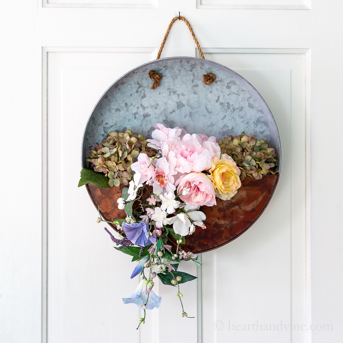 Metal galvanized hanging planter with flowers on white door.