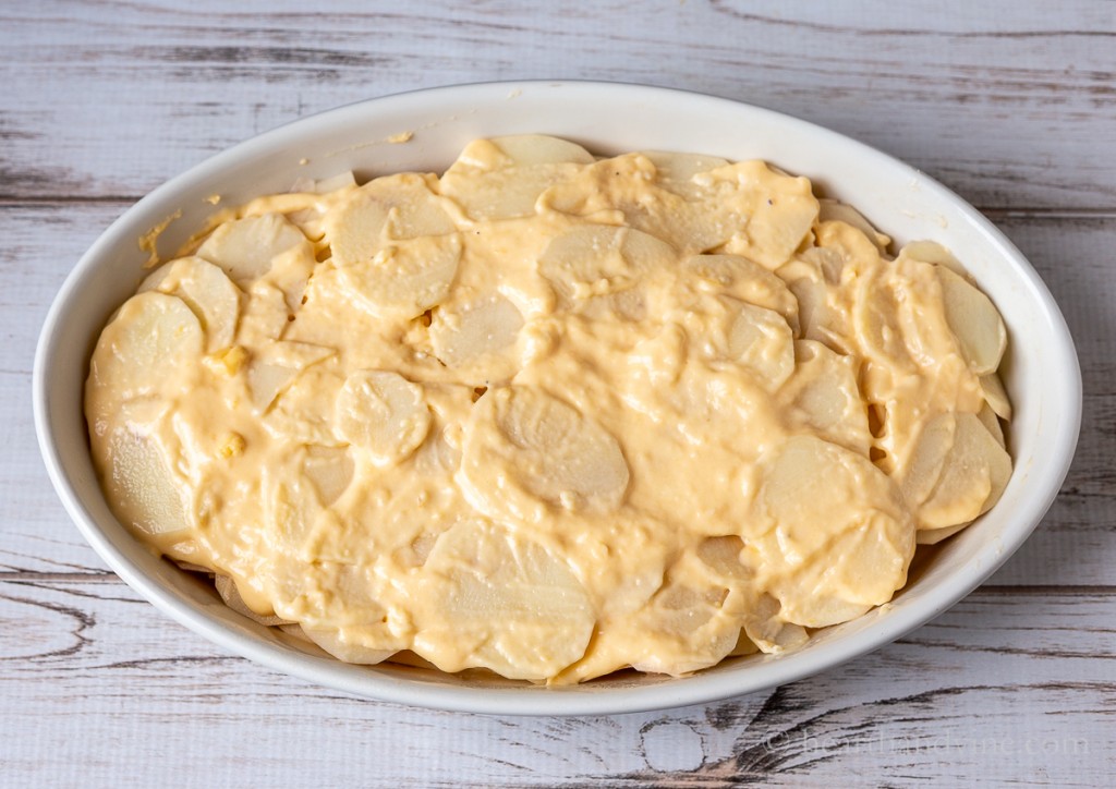 Potatoes and cheese sauce layered in a baking pan.