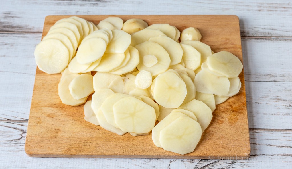 Thinly sliced potatoes on a wooden cutting board.