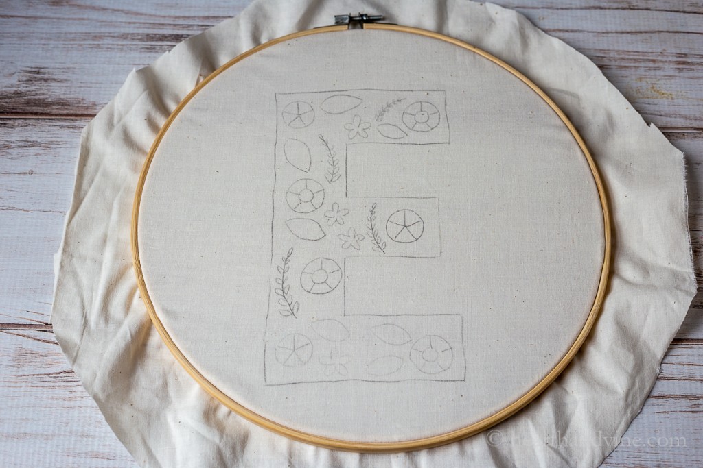 E monogram with embroidery shapes on muslin in a large embroidery hoop.