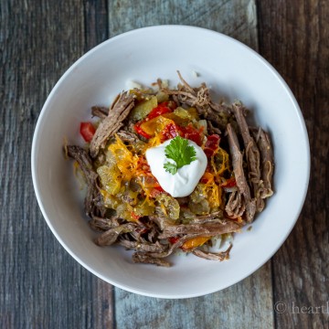 Bowl of carne asada over cauliflower rice with cheese, tomatoes and sour cream on top.