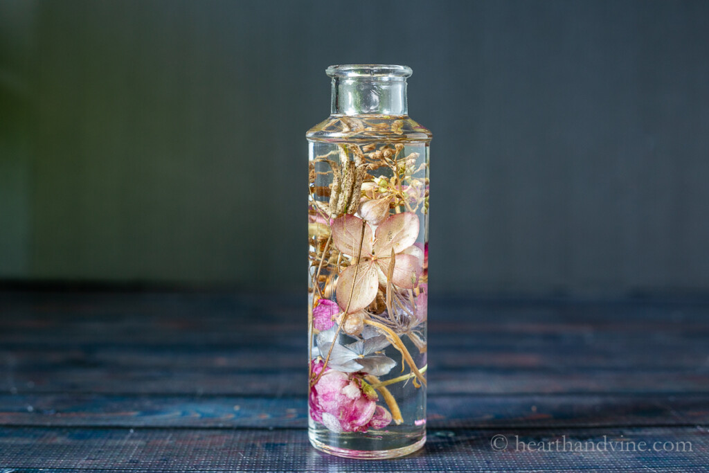 Dried flowers in oil in a tall glass jar.