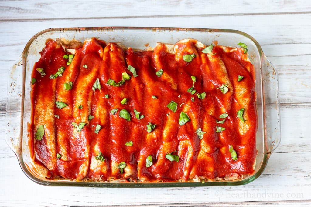 Casserole baking dish with Crepini filled cannelloni topped with tomato sauce and fresh basil.