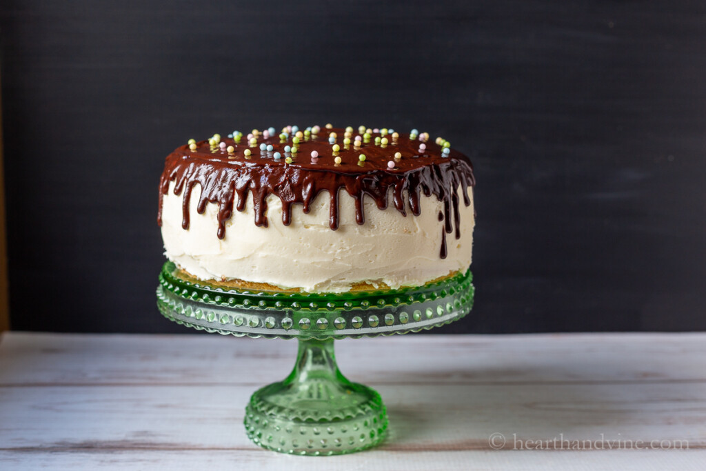 Two layer chocolate drip cake on a green glass cake stand.