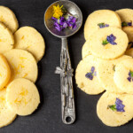 Violet and dandelion cookies on a black tray with a ornate silver spoon in the middle