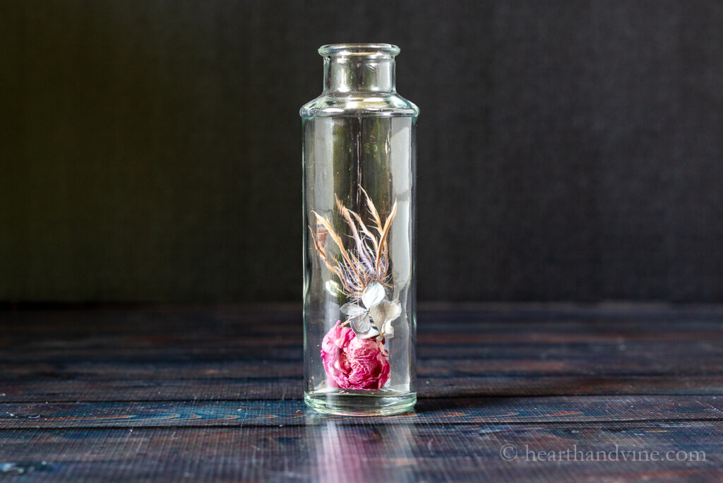 Glass bottle with a few dried flowers inside.