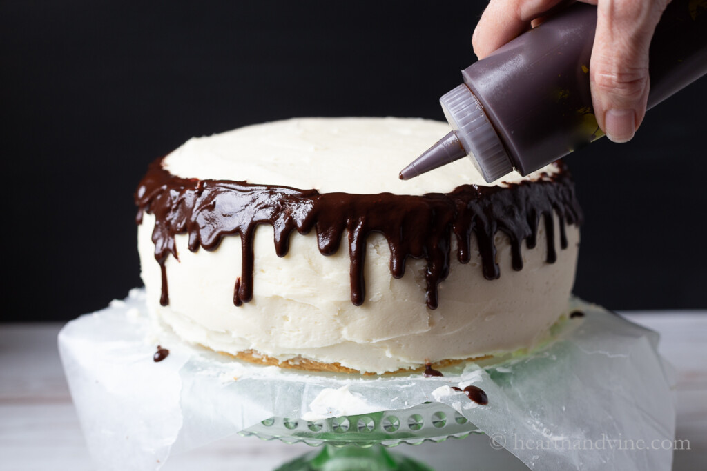 Chocolate drip ganache poured from a squeeze bottle on the edge of a two layer white cake.