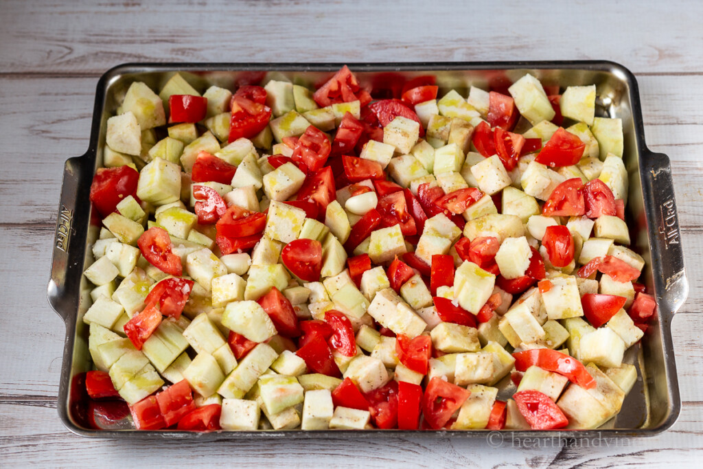 Cube eggplant, chopped tomatoes and a few garlic cloves on a large baking sheet pan.