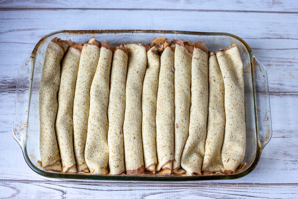 Glass casserole dish with twelve stuffed crepes.