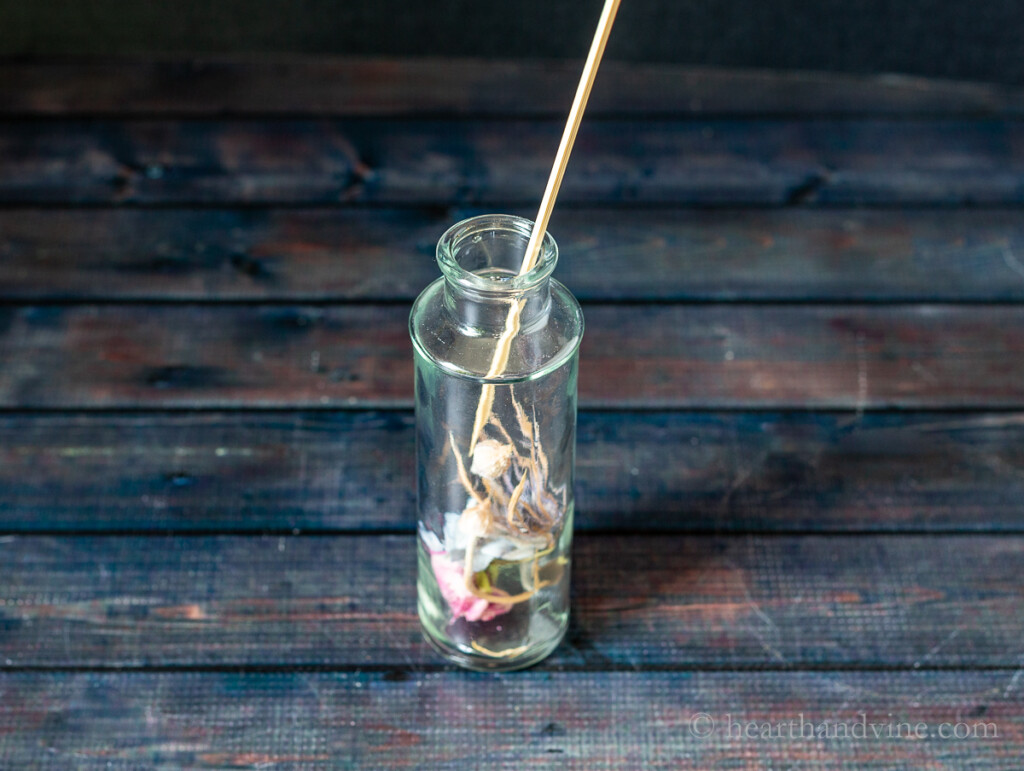 Glass bottle with a few dried flowers inside. A wooden skewer is used to position flowers.