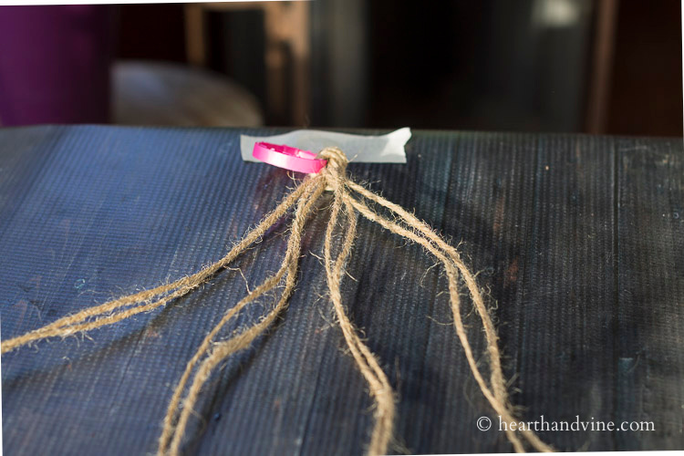 Eight lengths of twine tied together to a plastic ring that is taped to a table. They are separated into groups of two.