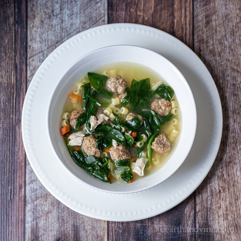 Bowl of wedding soup with meatballs, chicken, pasta, and spinach.