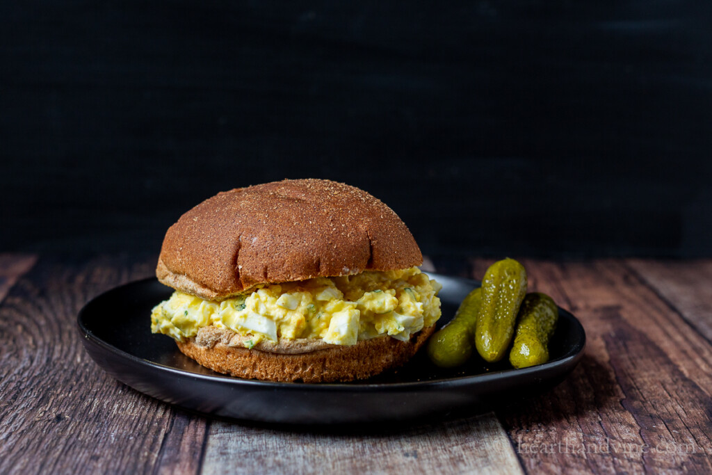 Greek yogurt egg salad sandwich with dill pickles on the side.