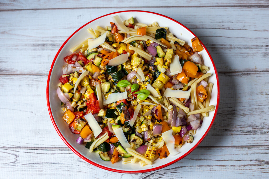 Grilled vegetables tossed with short pasta and grated Parmesan cheese in a large serving bowl.