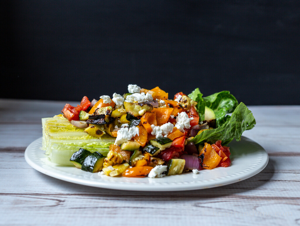 Grilled vegetable salad plate with romaine lettuce wedge topped with chopped vegetables and goat cheese crumbles.