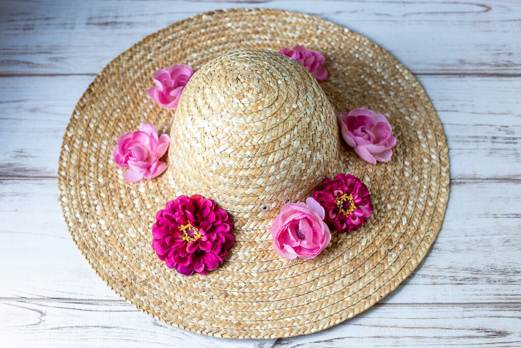 Large straw hat with a few large pink and fuchsia colored fake flowers around the rim.