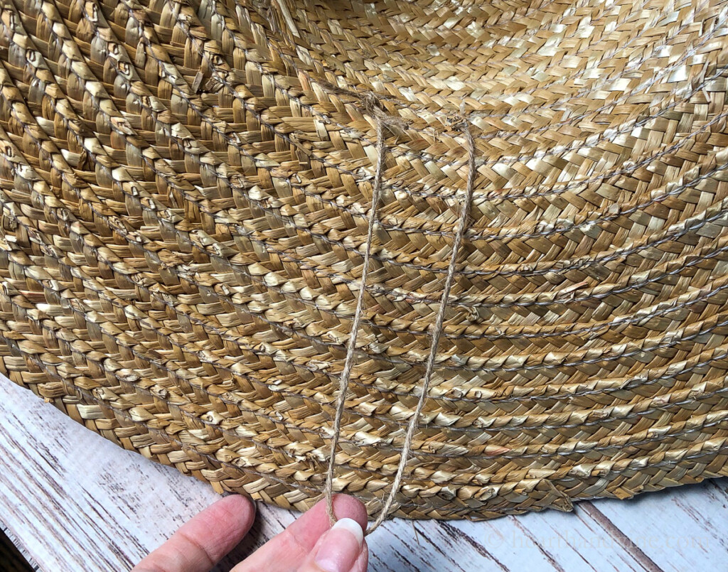 Piece of jute threaded through straw hat rim.