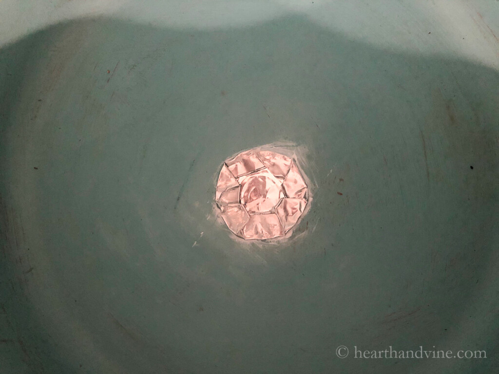 A tealight metal container is smashed and glued to the hole in a clay pot.