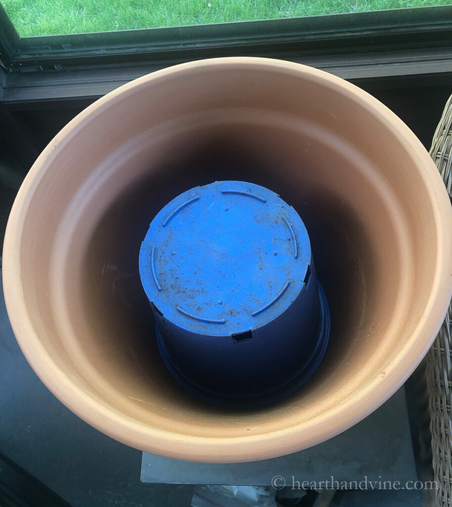 A blue plastic pot set upside down inside a large clay pot.