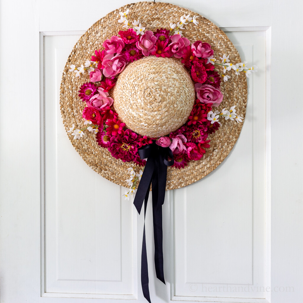 Straw hat with pink flowers on a white door.