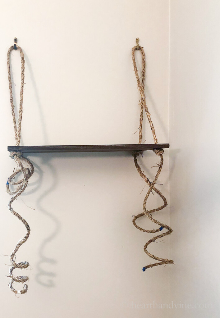 Floating shelf with rope on picture hangers and extra rope below.