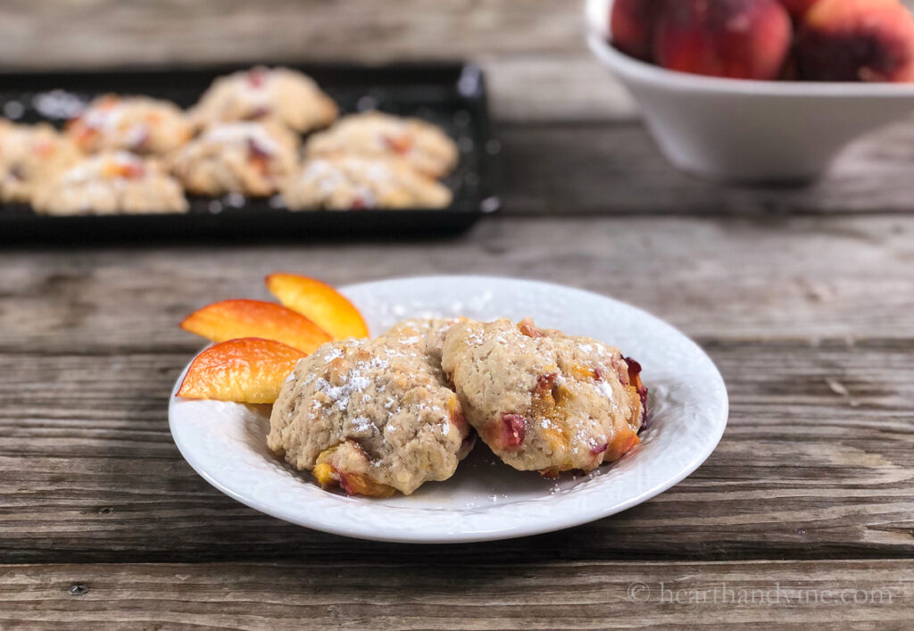 Two baked peach fritter on a plate with slices of peaches on the side.