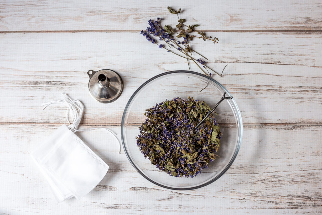 Bowl of dried lavender and lemon balm. A small metal funnel and a stack of tea filter drawstring bags.