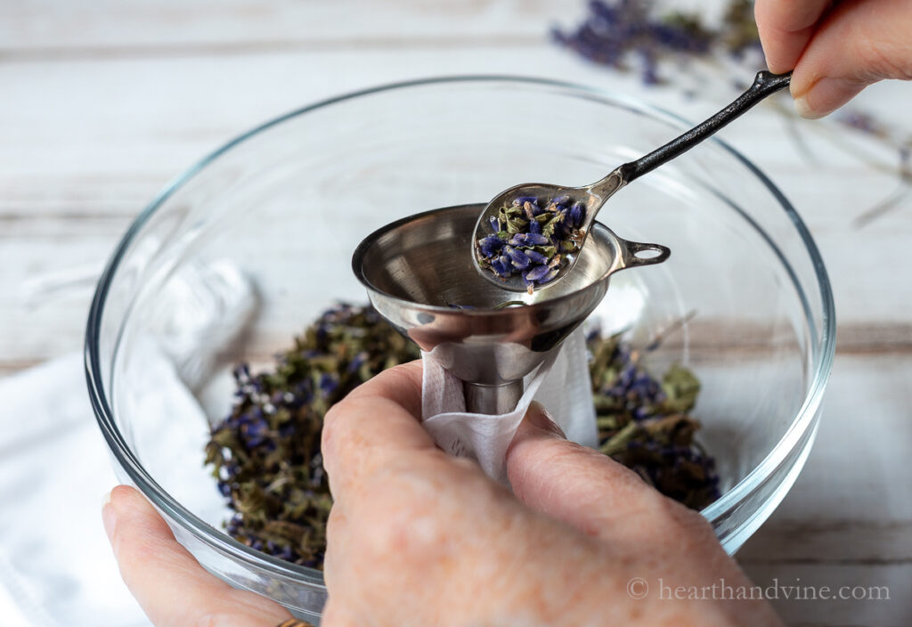 Filling small bags with a metal funnel and a small spoon with dried lavender and lemon balm.
