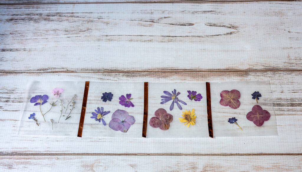 Four wax paper pressed flower parts with strips of metallic tape connecting the sides.