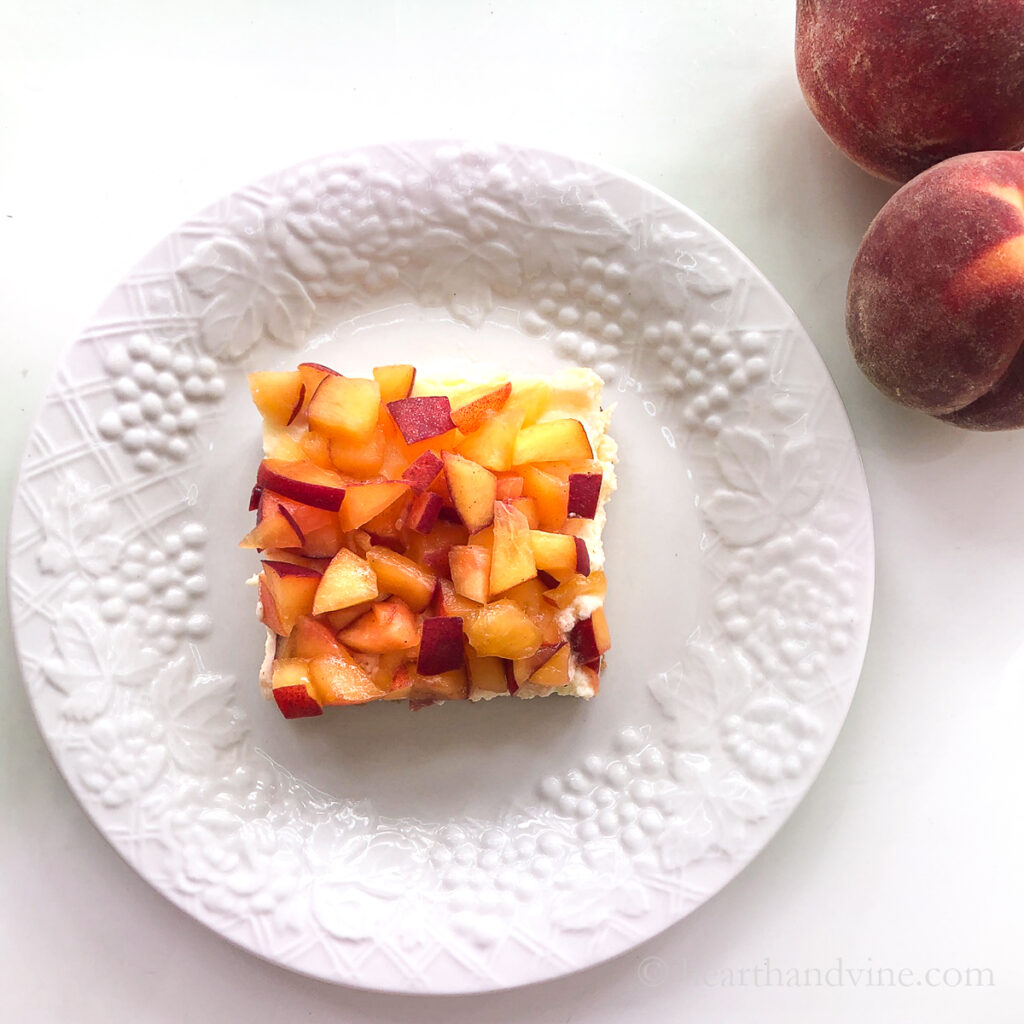 Fresh ginger peach cheesecake bar serving on a plate with whole peaches on the side.