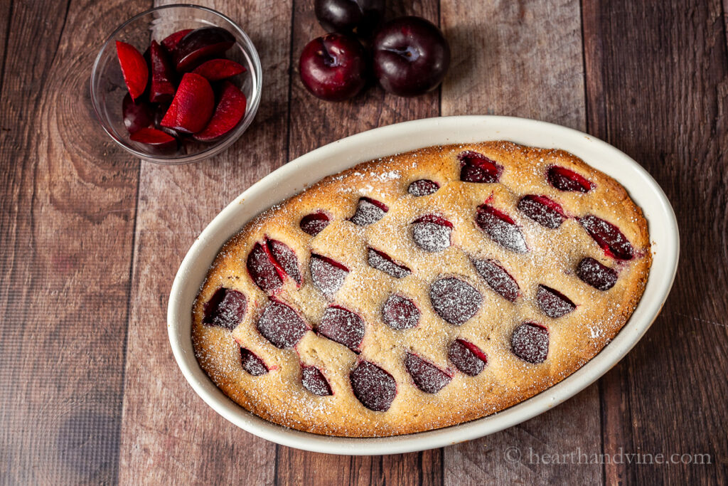 Oval ceramic pan with plum cake dusted with powdered sugar.