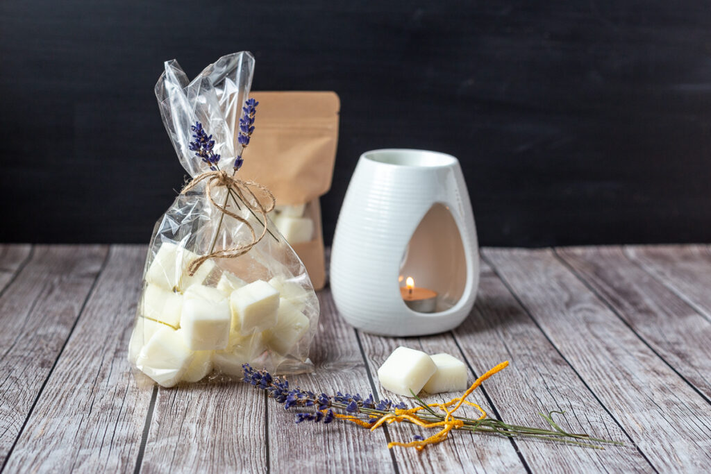Bag of wax melts next to a wax burner with a tealight and some dried lavender and lemon peels.