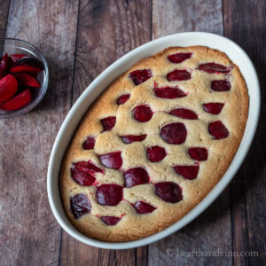 Fresh plum cake in a large baking dish next to a bowl of fresh plums.