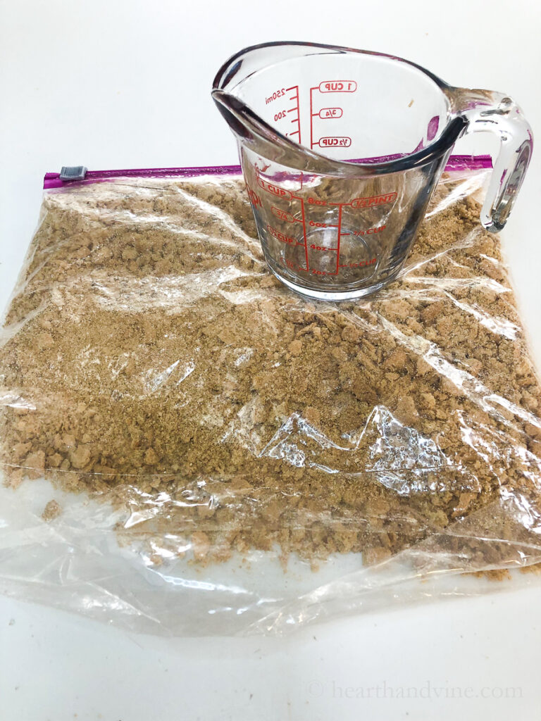 Plastic bag of graham crackers and a glass measuring cup on top used to crush the crackers.
