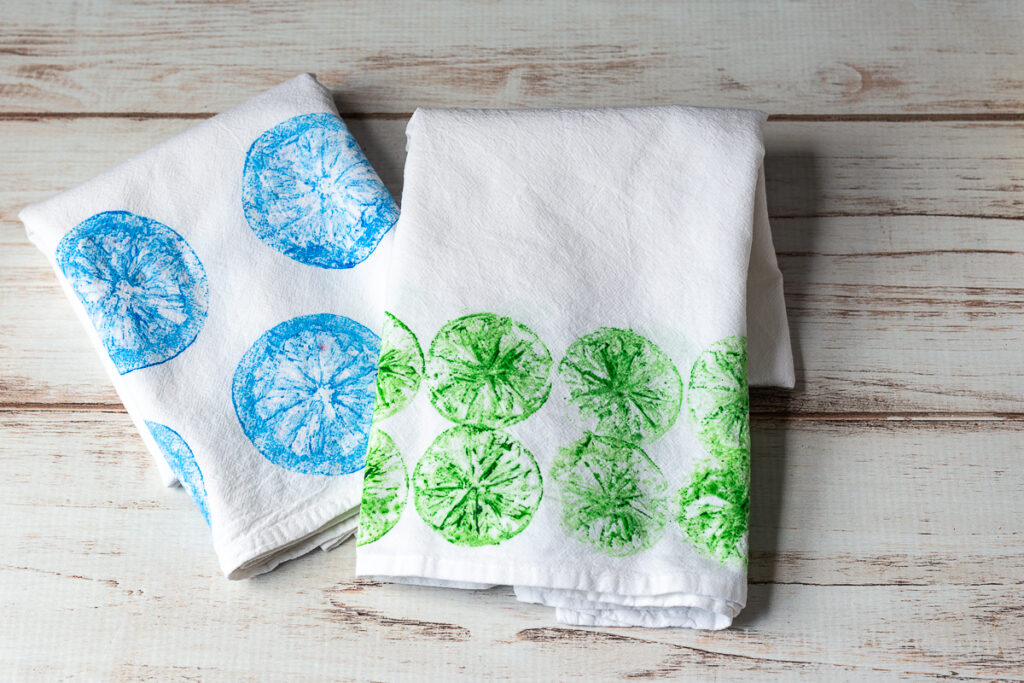 Green and blue fruit prints on two flour sack towels.