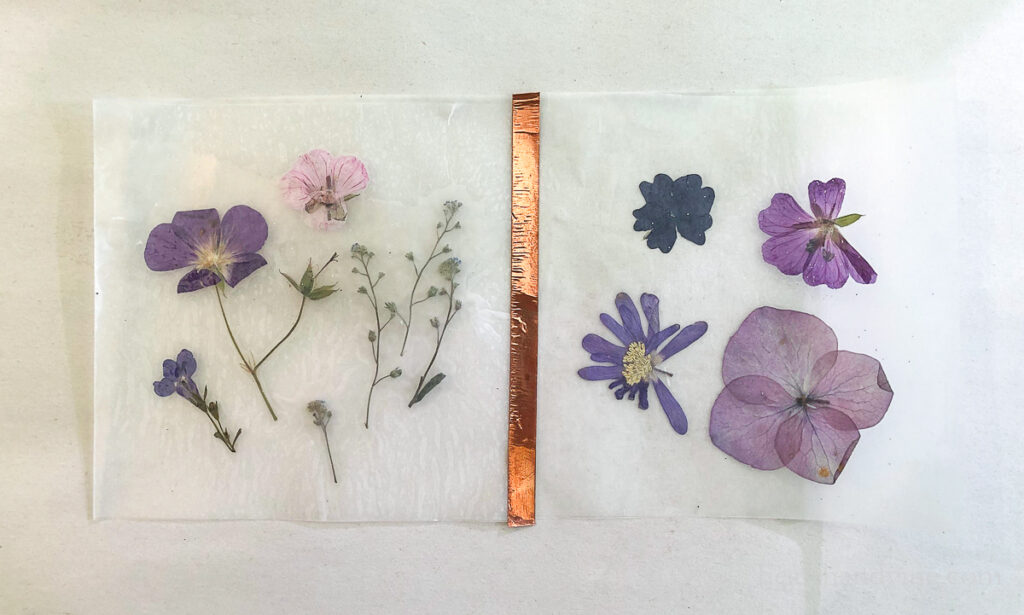 Two squares of pressed flowers between wax paper. A strip of copper tape holding to sides together.