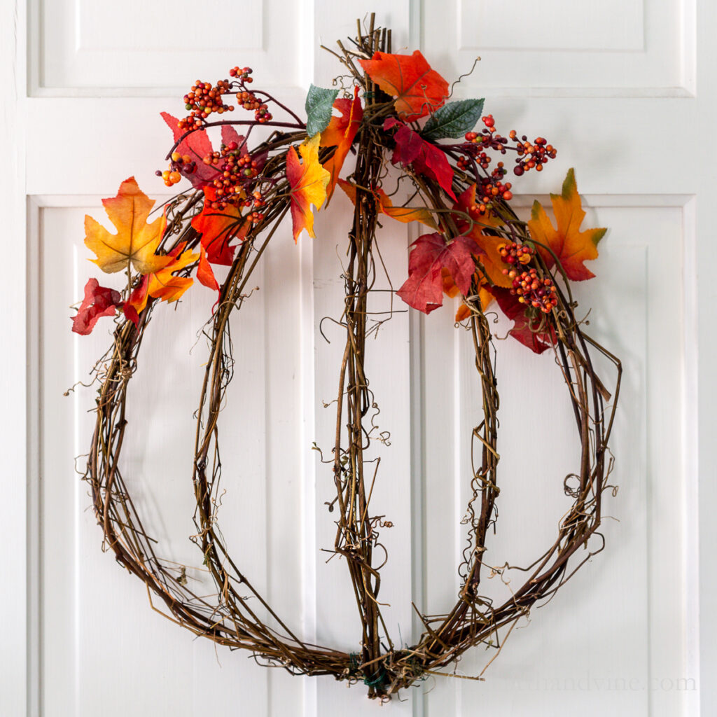 Grapevine wreath in a pumpkin shape with fall leaves and berries.