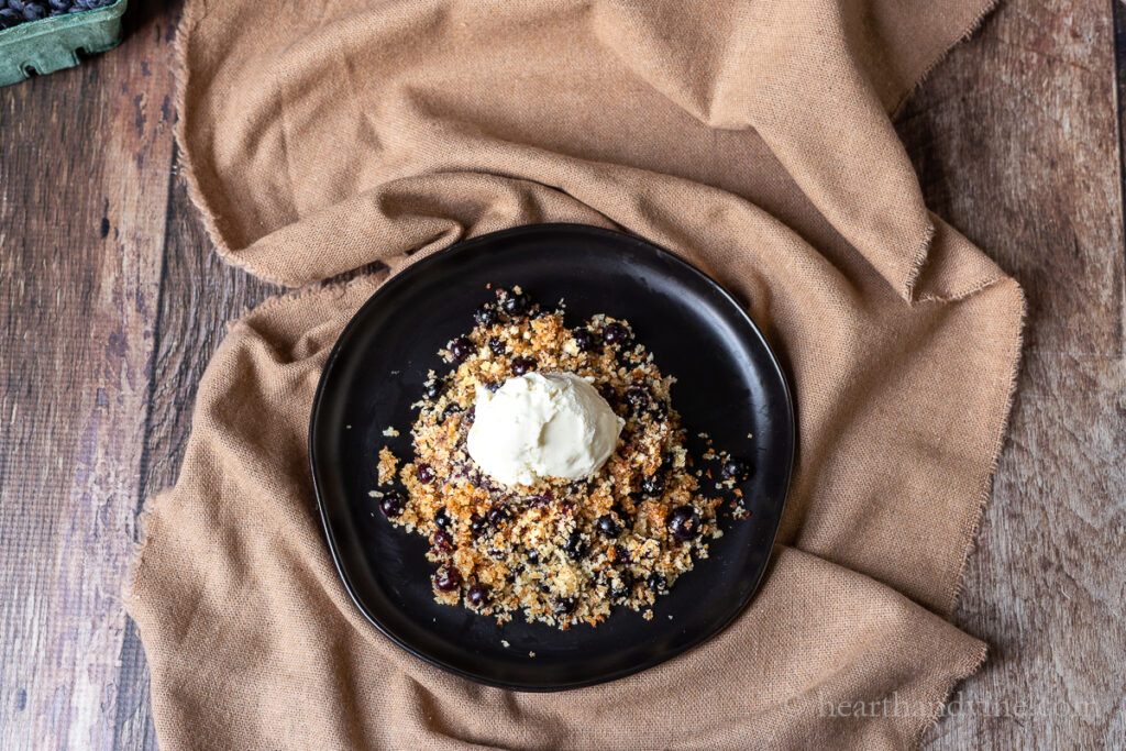 A serving of blueberry brown Betty on a plate with vanilla ice cream.