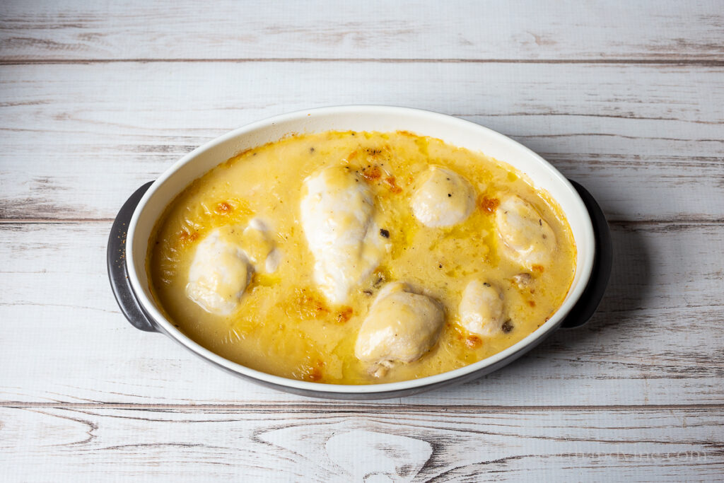 Baked chicken parts with sauce out of the oven in a large baking pan.