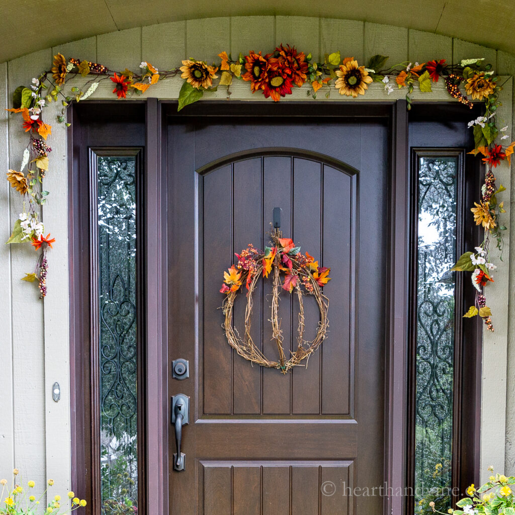 Fall decorated front door with a pumpkin wreath and fall garland