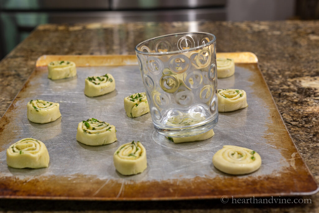 Puff pastry pinwheels on a cookie sheet and a glass flattening them.