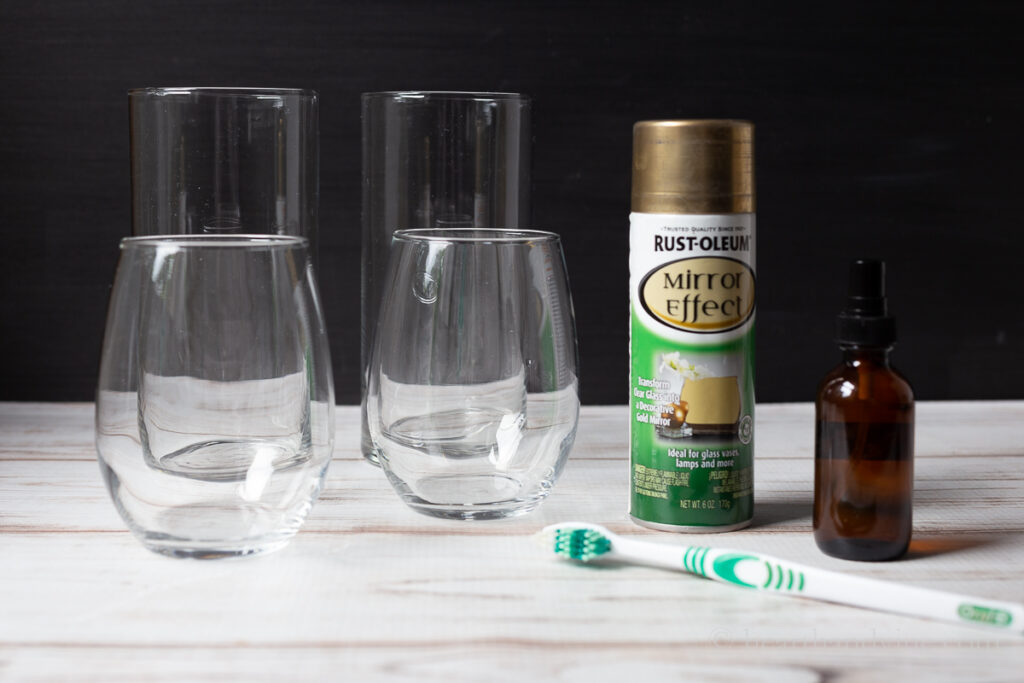 Four glass vases. Two smaller and rounded and two tall and straight. A can of mirror spray paint in gold. A small amber spray bottle and an old toothbrush.