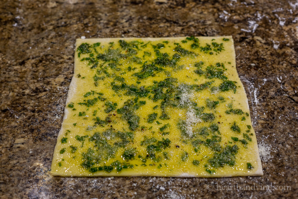 Fresh chopped herbs, parmesan cheese and oil spread on a puff pastry sheet.