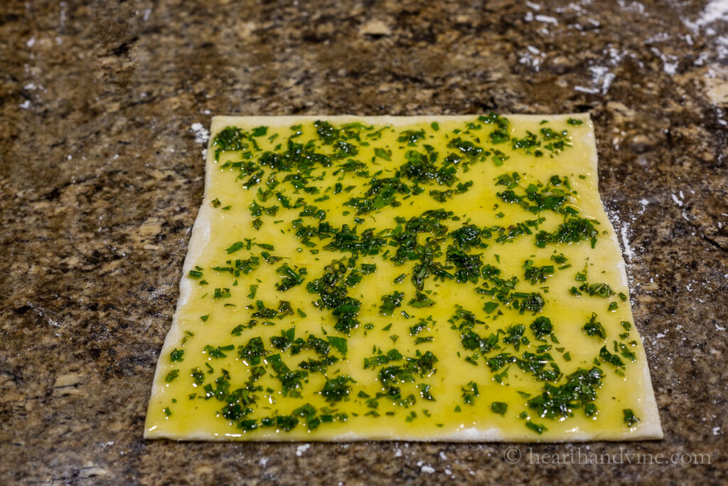 Fresh chopped herbs and oil spread all over a puff pastry sheet.