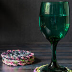 Green wine glass on fabric coasters next to a stack of fabric twine coasters