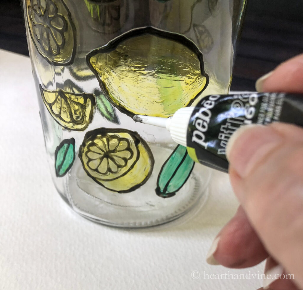 Using black paint outliner on bottle to outline glass paint pattern.