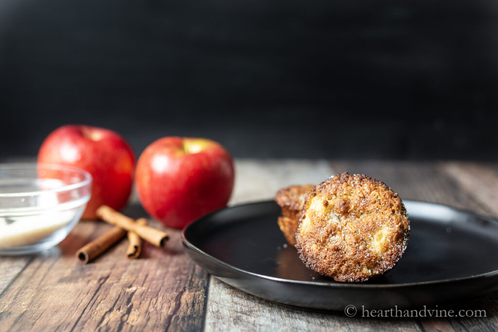 Apple oat muffins on a plate next to some apples and cinnamon sticks.